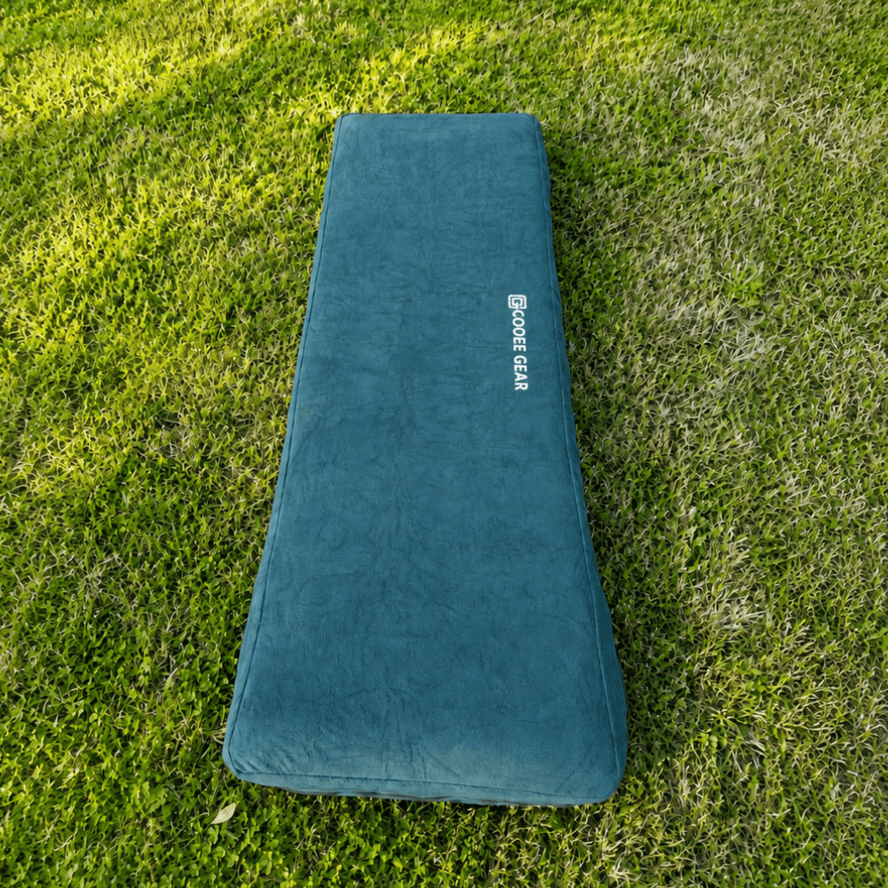 A dark teal outdoor sleeping pad with a white 'Cooee Gear' logo, laid flat on a green grass lawn.